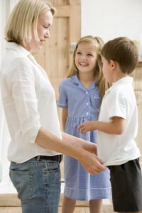 Woman in front hallway with two young children smiling